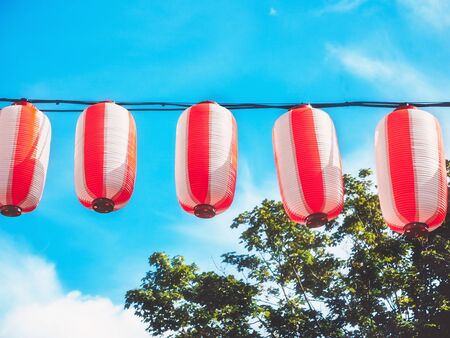 Paper red-white japanese lanterns Chochin hanging on blue sky background. Summer background