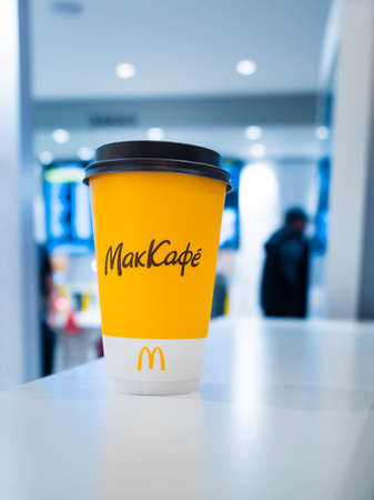 Moscow, Russia - April 3, 2021: One yellow cup of coffee on the table at Mcdonalds, people stand at the customer service counter on background. The inscription in Russian McCafeのeditorial素材