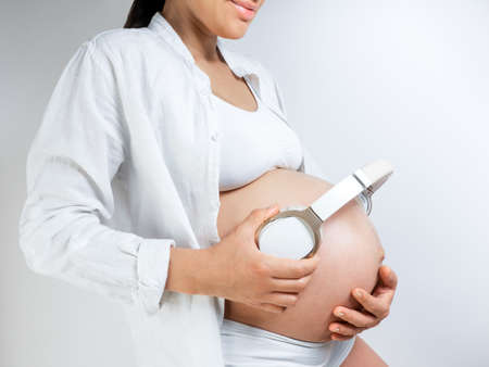 Pregnant woman music lover put the headphones on her belly to let Rebecca enjoy the music she likes. Girl waiting for a baby keeps headphones on her stomachの写真素材
