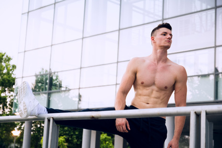 Young man stretching his leg after a heavy workout. Wearing tracksuits without shirt. Selective focus.の写真素材