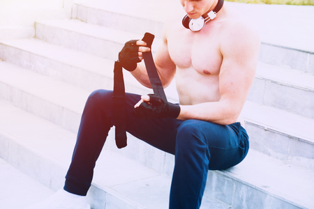 Young male preparing for hard workout and putting his gloves for training. Wearing tracksuit without shirt. In the backgroung modern sport centar. Selective focus.の写真素材