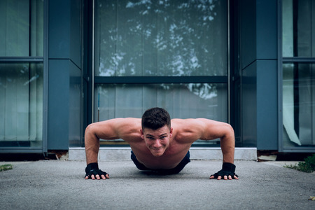 Young male doing push ups in front of the modern sport center. Selective focus.の写真素材