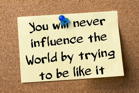 You will never influence the World by trying to be like it - adhesive label pinned on bulletin board - horizontal imageの写真素材