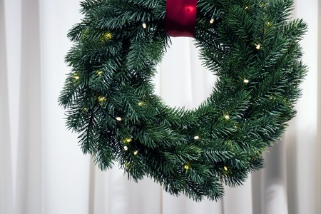 Christmas fir-tree wreath with red tape illuminated by garlandの写真素材