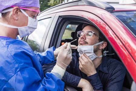 A doctor in a protective suit taking a nasal swab from a person to test for possible coronavirus...