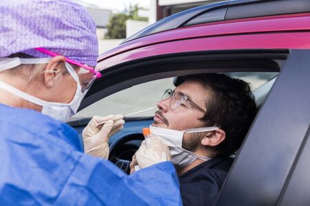 A doctor in a protective suit taking a nasal swab from a person to test for possible coronavirus...
