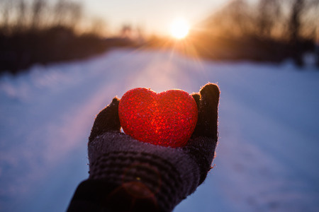 Abstract heart on hand with snow in the rays of the sunset.