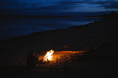 Silhouette of tourist girl around the campfire at night on the river shore.