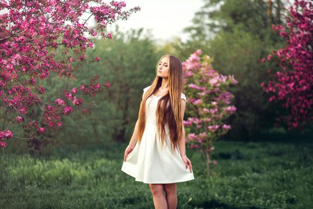 Beautiful blonde girl in pink peach and sakura garden. Beautiful girl outdoors spring portrait, young woman with flowers in green park spring concept.の写真素材