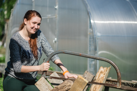 Happy girl is sawing a wooden beam the hand saw in the garden.