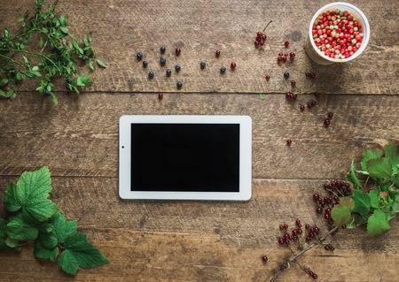 Workspace. Composition with tablet pc and bilberries, red currant with leaves in the old wooden impressive boards. Natural light shadows.の写真素材