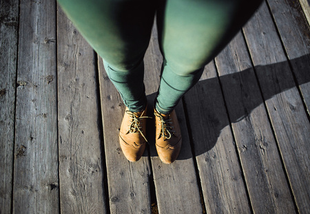 Female feet in brown boots and green pants on wood background. Walking fashion hiking concept.の写真素材