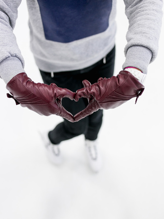 Closeup of young girl shows abstract heart symbol by leather gloves on ice. Concept of love to...