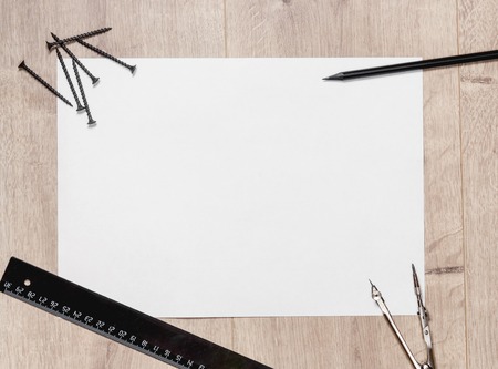 Flat composition of empty drawing sheet and screws, a ruler, a compass on wooden tableの写真素材