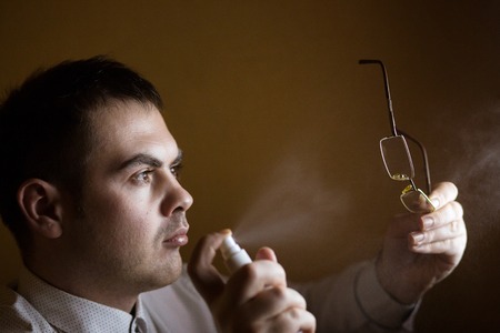 Man cleaning a spray pair of reading glasses spectacles