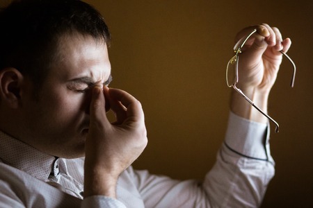 Man with tired eyes after long work holding his eyeglasses.の写真素材