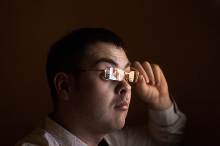 Young attractive businessman alone at night sitting at computer laptop watching porn or online gambling which reflecting in his glasses isolated on black background on internet chat addiction concept.の写真素材