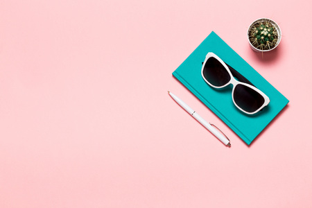 Creative flat lay photo of workspace desk with aquamarine notebook, eyeglasses, cactus copy space pink background, minimal style.の写真素材