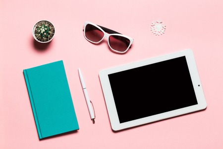 White tablet, green-blue diary, white pen, glasses, snowflake, and cactus on pink background. flat lay composition, top view. Feminine workspace. Winter focus.の写真素材