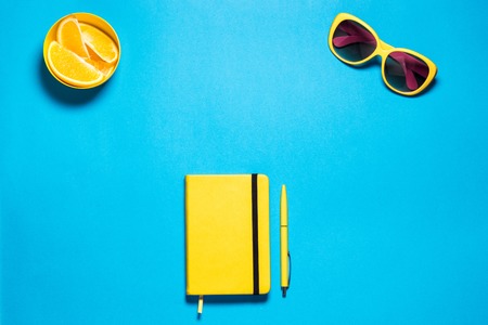 Stylish minimalistic feminine fashion workspace. Bright yellow glasses and diary with pen, pirces oranges against deep blue copy space. Top viewの写真素材