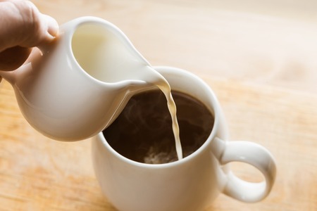 Pouring Cream into a White Cup of Hot Morning coffee. Beautiful Soft Light.の写真素材