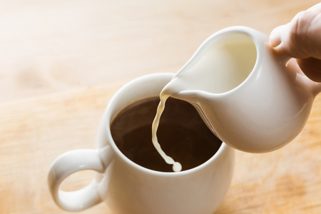 Pouring Cream into a White Cup of Hot Morning coffee. Beautiful Soft Light.の写真素材