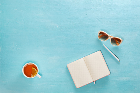 Opened notebook with pen, cup of tea and sunglasses on blue wooden table. Top view. Writing, blogging concept.の写真素材