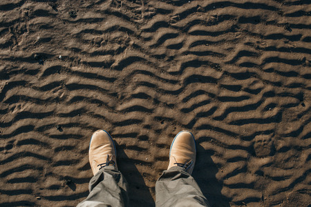 Top view of legs and beige suede boots standing on the beachの写真素材