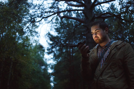 Man has got lost in the wood looks in phone in the evening. Concept of navigation, loneliness,...