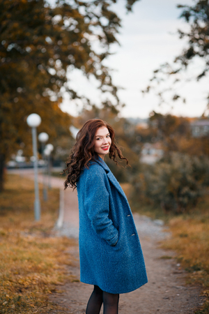 Romanric picture of fashionable young curly woman in autumn in park smiling and turning wearing blue coat. Girl turned with fluttering hair.の写真素材
