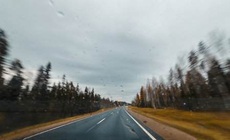 Autumn forest road at high speed drive. View from windscreen with drops.Travel concept.の写真素材