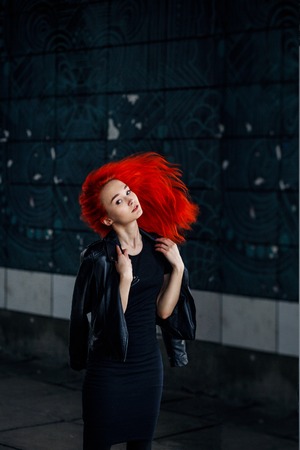 Expressive Redhead woman posing at dark wall and her hair flying against black background.の写真素材