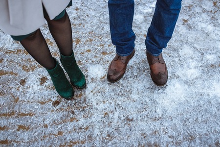 Winter is coming. Female and male boots on rough ice surface. Top view. Two friends or lovers standing on beach covered fresh ice.の写真素材