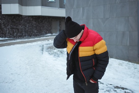 Handsome young man outdoor in colorful winter jacket looking away at cold gray urban backgroundの写真素材