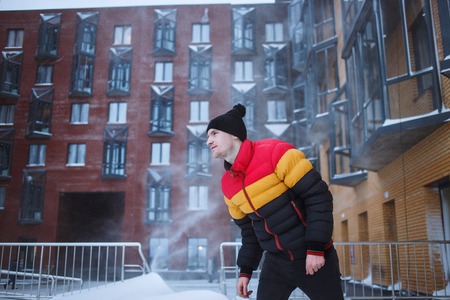 Strong man with in winter clothes enjoys the snow, cold, snowfall, blizzard. Urban yard backgroundの写真素材