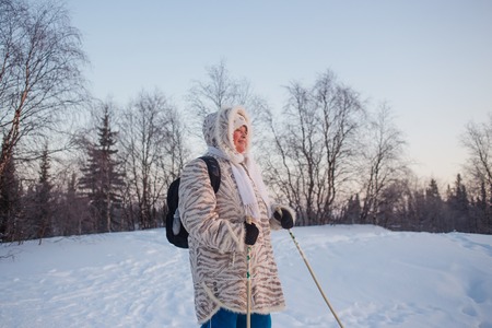 Happy senior woman looking to winter sunset in forest. Nordic walking activityの写真素材