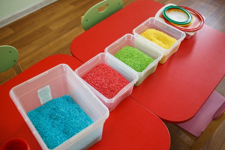 Sensory bin for toddlers with colourful rice on red table.の写真素材