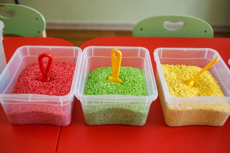 Sensory bin for toddlers with colourful rice on red table.の写真素材