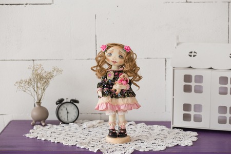Portrait of textile handmade vintage doll with green eyes, long brown curly hair in light pink and blue textile dress with gentle print, in on white background. She holding little textile teddy bearの写真素材