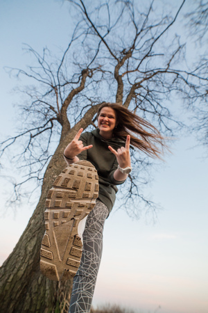 Urban style and fashion concept. Outdoor portrait of beautiful stylish young European female model with long brown hair wearing trendy hoodie and white sneackers watches, posing in evening autumn or spring park.の写真素材