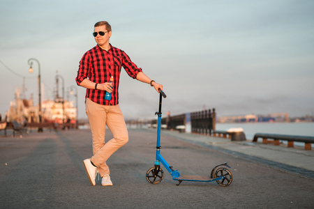 Pleasant smiling man posing with blue kick scooter and bottle of blue isotonic drinkの写真素材
