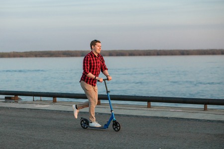 Young hipster man, riding on a kick scooter after work on sunset. Concept of healthy mobile transportの写真素材