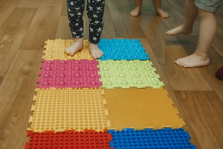 Toddlers on baby foot massage mat. Exercises for legs on orthopedic massage carpet. Orthopedic...