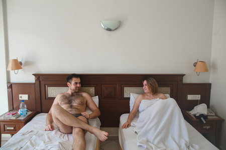 Happy young couple relaxing in hotel room. They lie in the next bed under the covers and look at each otherの写真素材