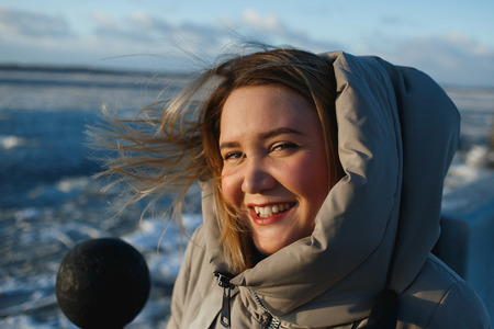 Portrait of pretty cheerful smiling woman on frozen river background in sunny winter day. Healthy winter walking in sinny frosty dayの写真素材
