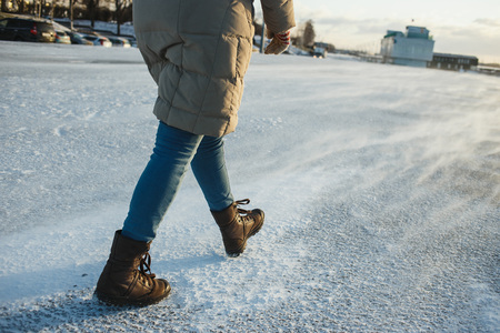 Woman in winter clothes going on cold winter street. Snowstorm sweeping, drizzle
