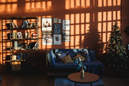 Arkhangelsk, Russia, November 26, 2018: Vintage christmas interior with a christmas tree bookcase, posters, photos and lettering in frames against the orange wall in the sunlightのeditorial素材
