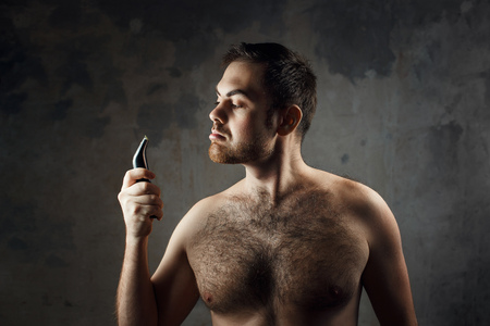 Hairy man with a naked torso holding an electric razor before shavingの写真素材