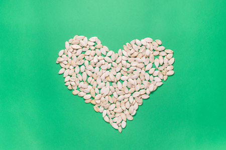 Heart shape of pumpkin seeds on green background. Minimalistic flat lay compositionの写真素材