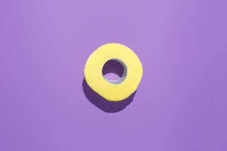 Yellow roll of toilet paper on a purple background. Flat composition